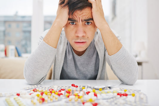 Man with anxiety sitting at table covered in red and yellow pills and holding his head